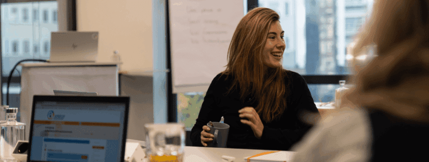 Vrouw aan tafel kijkt lachend naar rechts | AvA seminar GEO